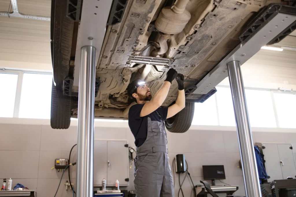 Mechanic inspecting a car exhaust system from underneath on a hoist